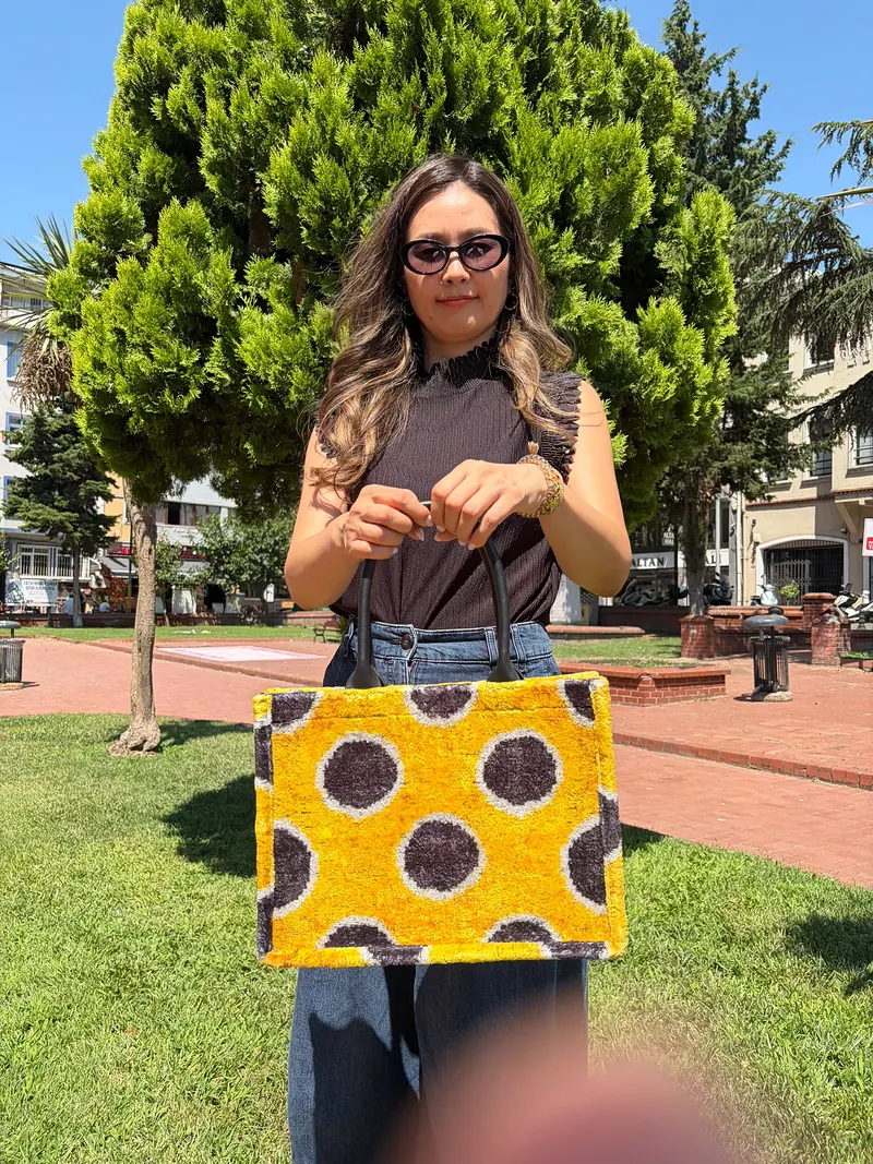 Saffron kilim tote with charcoal dots, held out by its rolled dark brown handles