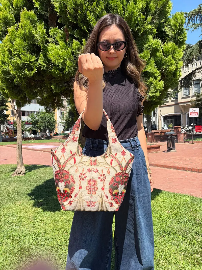The ivory-ground tulip bucket bag carried by its handles, showing its size against the body